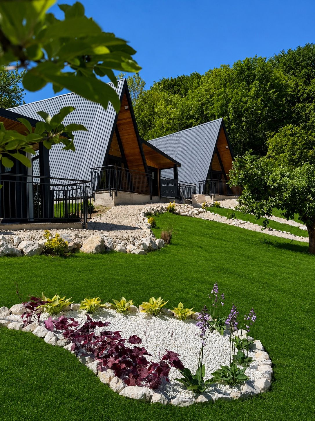 Două cabane A-frame negre în spatele unui strat de flori mărginit cu piatră de calcar.